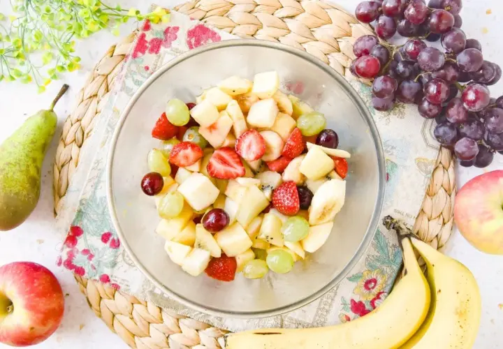 Un tazón lleno de colorida ensalada de frutas con fresas, uvas, plátano y trozos de manzana.