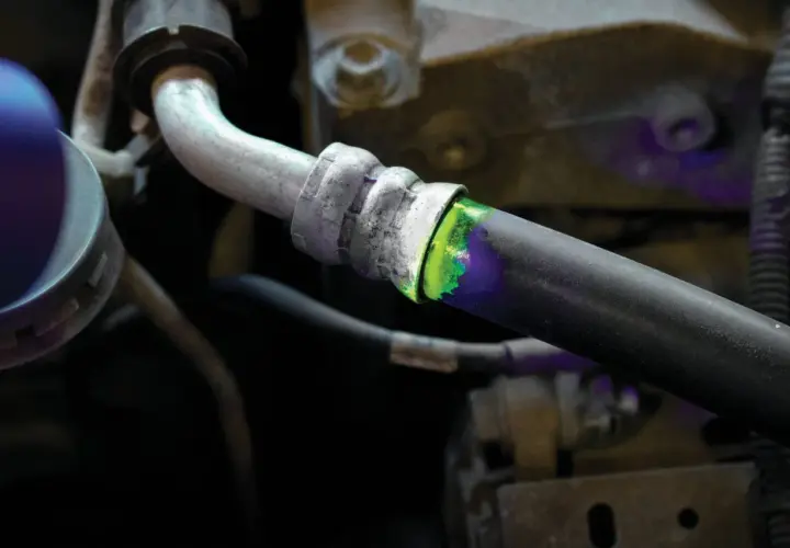 Detectando una fuga de aire en el sistema de aire acondicionado con tinte fluorescente verde y luz ultravioleta.