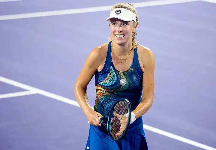 Uśmiechnięta hiszpańska tenisistka w sportowym stroju, z rakietą w dłoni, na fioletowym korcie.