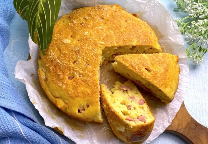 Torta salata prosciutto e formaggio dorata, con una fetta tagliata, su carta forno.
