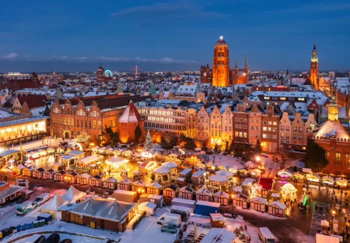 Gdańsk jarmark świąteczny nocą, z oświetlonymi kramami, karuzelą i zabytkową zabudową w tle.