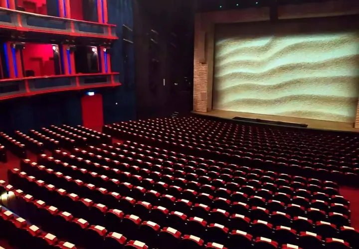 Puste rzędy czerwonych foteli w teatrze, z widownią i sceną z piaskowym tłem. Gdzie jest teatr Roma?