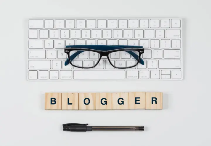 Klawiatura, okulary i drewniane klocki z napisem "BLOGGER".