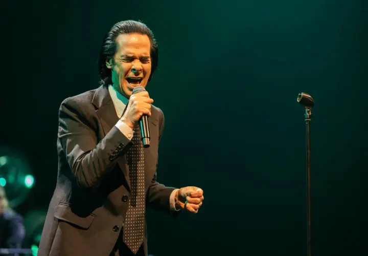 Nick Cave z pasją wykonuje swoje utwory, śpiewając do mikrofonu w eleganckim garniturze.