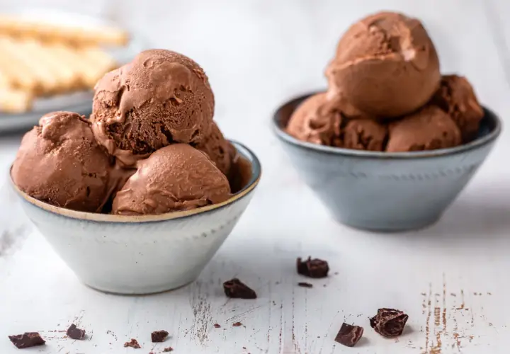 Due ciotole piene di cremoso gelato al cioccolato, con pezzi di cioccolato sparsi sul tavolo.