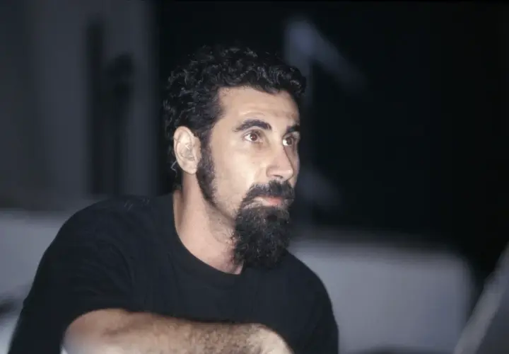 Serj Tankian, wokalista System of a Down, z charakterystyczną brodą i słuchawką w uchu, gotowy do wykonania kolejnych energetycznych utworów.