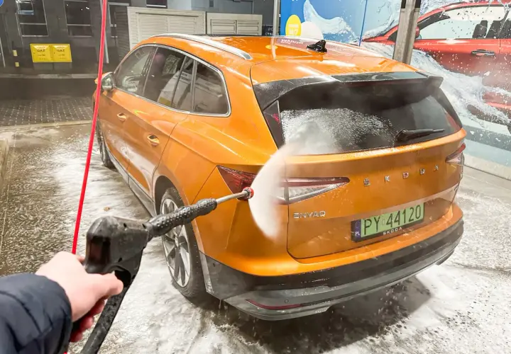 Jak dobrze umyć auto na myjni bezdotykowej? Pomarańczowa Skoda Enyaq jest spryskiwana wodą pod ciśnieniem.