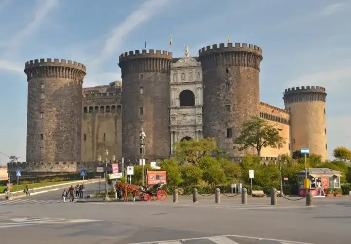 Castel Nuovo w Neapolu, imponująca forteca z wieżami i bramą, to jedno z miejsc, które warto zobaczyć. Obok przejeżdża dorożka.