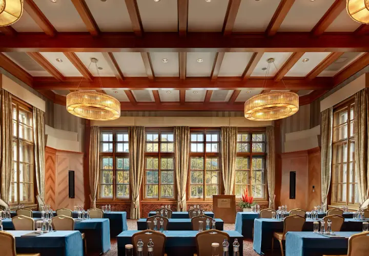 Elegancka sala konferencyjna w Kempinski Hotel, z drewnianymi belkami na suficie, dużymi oknami z widokiem na jesienny krajobraz i stylowymi żyrandolami.