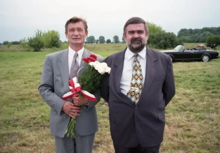 Wspólnik kilera z komedii Machulskiego, z bukietem kwiatów, obok kolegi i czarnego kabrioletu na łące.