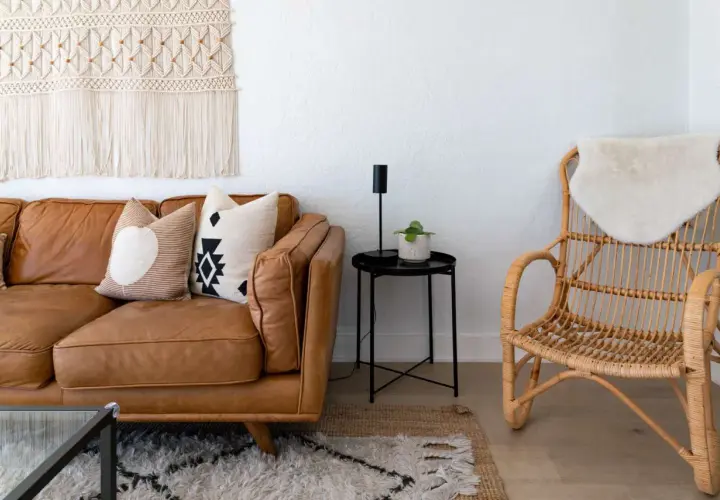 A cozy living room with a brown leather sofa, patterned pillows, a macrame wall hanging, and a rattan chair, embodying a relaxed bohemian furniture style.