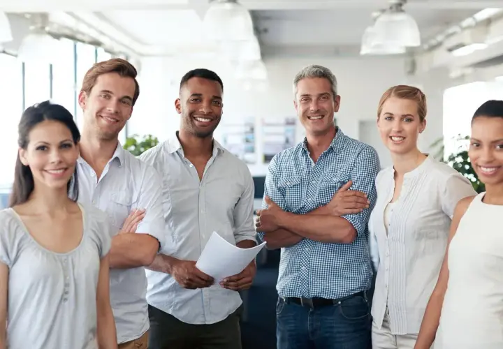 A diverse team smiles confidently, showcasing what employee engagement looks like. They stand together in a bright office, radiating positivity and collaboration.
