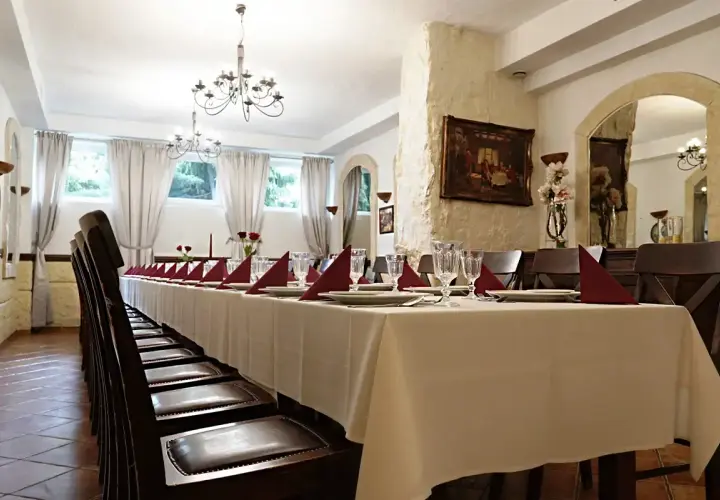 Długi stół w restauracji, nakryty białym obrusem, z czerwonymi serwetkami i kieliszkami. Czy rezerwacja stolika w restauracji jest płatna?