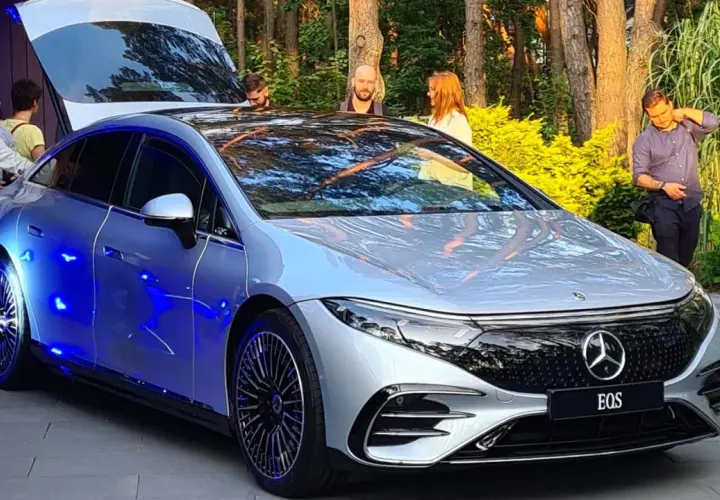 Srebrny Mercedes EQS z niebieskim podświetleniem prezentuje się efektownie na tle zieleni.