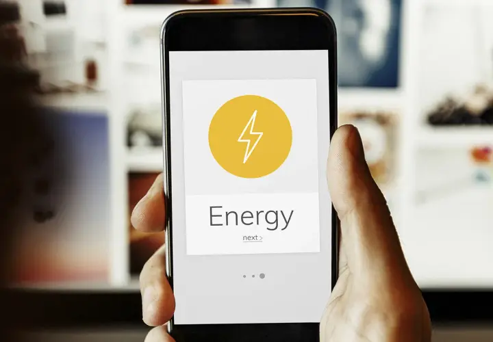 Mano sujetando un smartphone con una app de monitorización energética. El icono de un rayo y la palabra "Energy" indican el control del consumo.