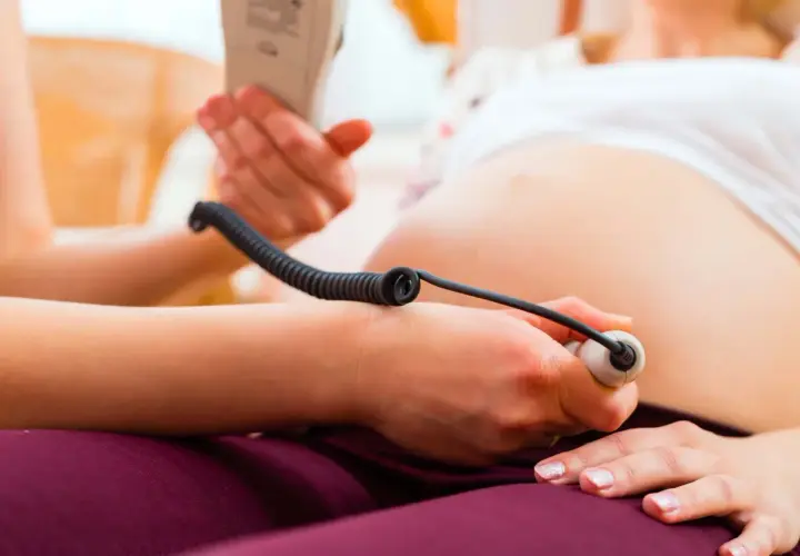 En barnmorska lyssnar på ett barns hjärtljud med en doppler. En del av en gravid mage syns. Inskrivning gravid.