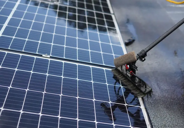 Brosse rotative en action pour nettoyer panneau solaire. L'eau ruisselle sur les cellules bleues et brillantes.