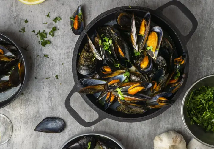 Una deliciosa preparación de mejillones, mostrando que son los mejillones, servidos en una sartén negra con perejil fresco y limón.