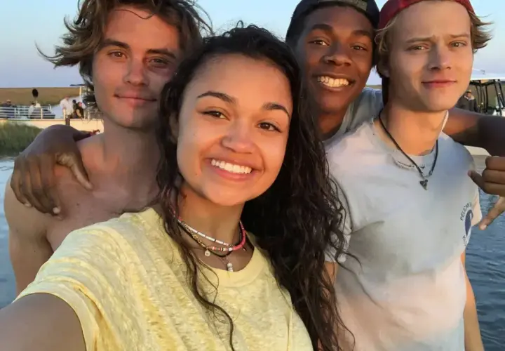 Uśmiechnięta **outer banks obsada** pozuje do selfie na plaży.