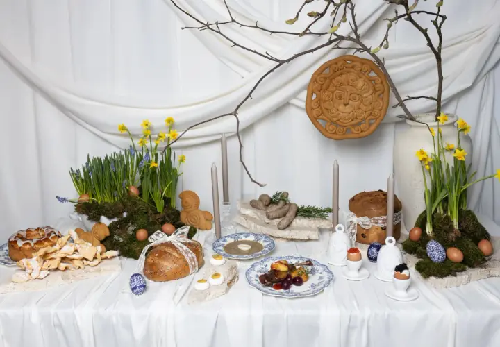 Wielkanocna oferta cateringowa: stół z tradycyjnymi potrawami, babkami, chlebem, jajkami i wiosennymi kwiatami.