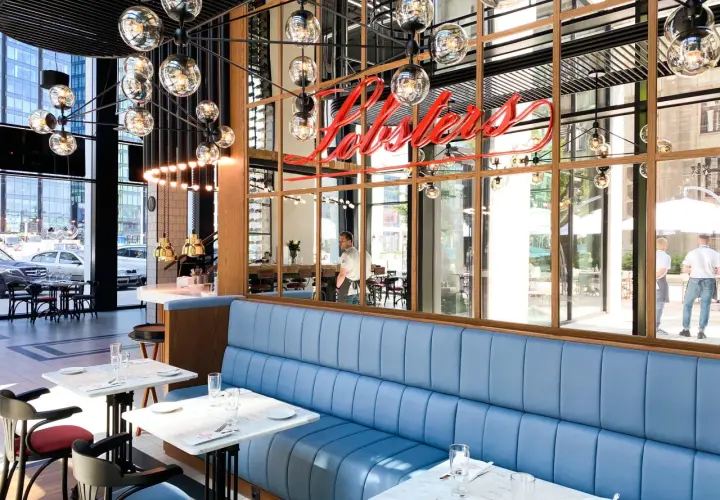 Elegancka restauracja z owocami morza w Warszawie. Neonowy napis "Lobster" nad błękitnymi kanapami.
