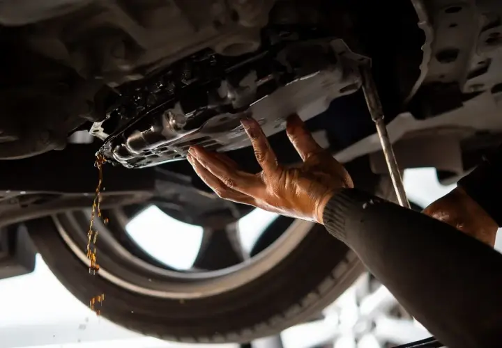 Mechanik spuszcza olej z miski olejowej. Dowiedz się, ile kosztuje wymiana oleju u mechanika.