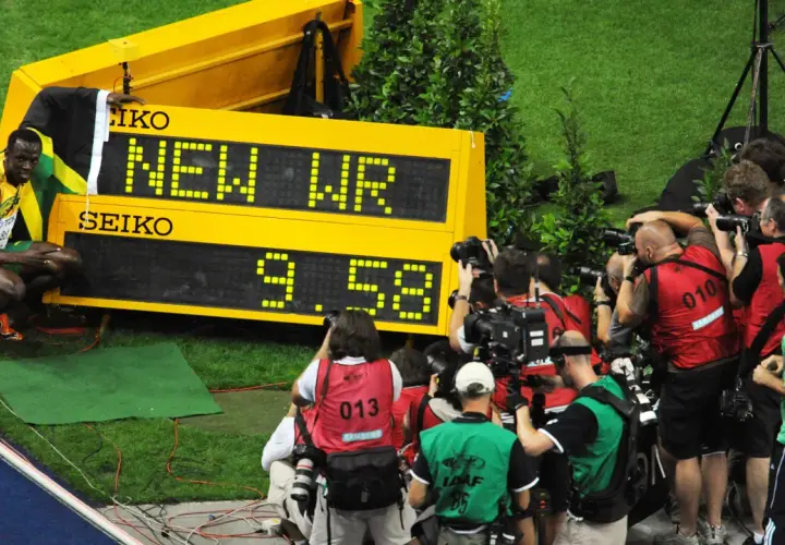 Usain Bolt, najszybszy człowiek świata, świętuje nowy rekord świata 9.58s. Otoczony przez fotoreporterów, z flagą Jamajki.
