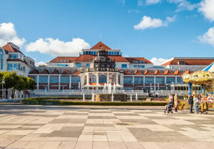 Sopot, część Trójmiasta, co to za miejsce? Plac z karuzelą i fontanną przed pięknym budynkiem.