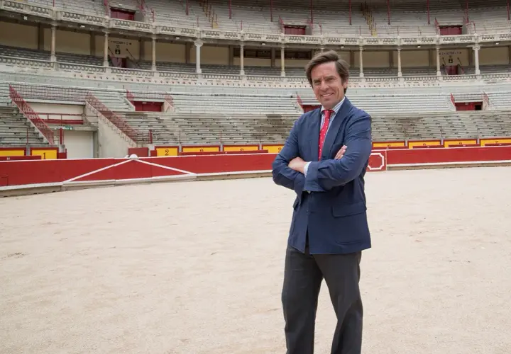 Eduardo Dávila Miura, con traje azul y corbata roja, posa en el ruedo de una plaza de toros.