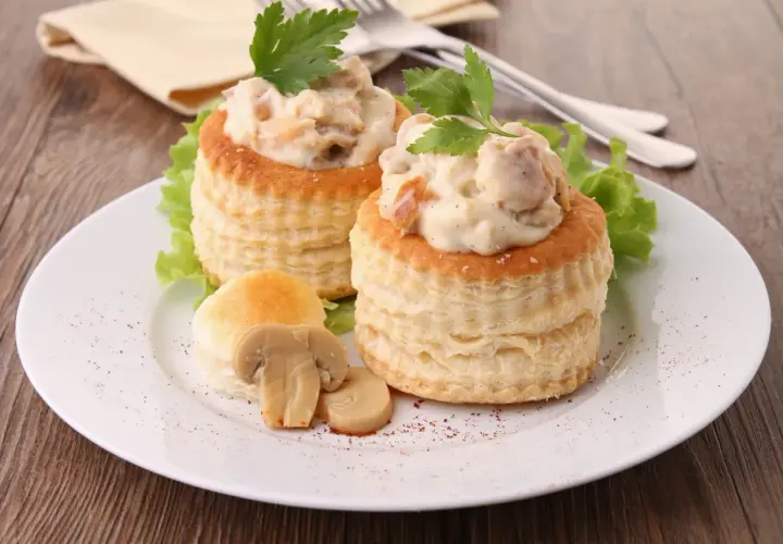 Deux vol-au-vent poulet crémeux, garnis d'une sauce onctueuse et de morceaux de poulet, décorés de persil frais et accompagnés de champignons.