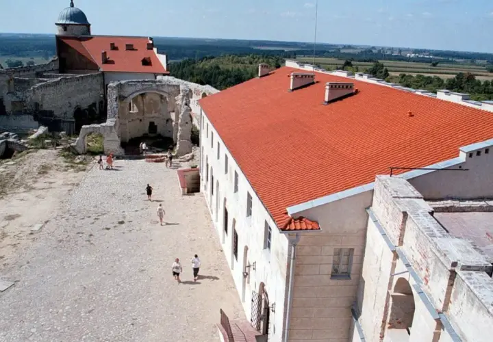 Dziedziniec zamku w Janowcu z ruinami i odrestaurowanym budynkiem z czerwonym dachem.
