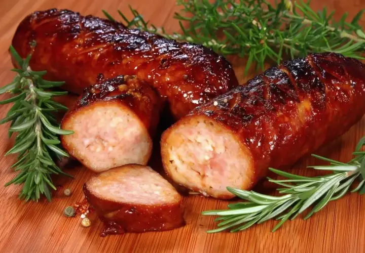 Soczysta kiełbasa z piekarnika, rumiana i aromatyczna, z gałązkami rozmarynu i ziarnami pieprzu na desce.
