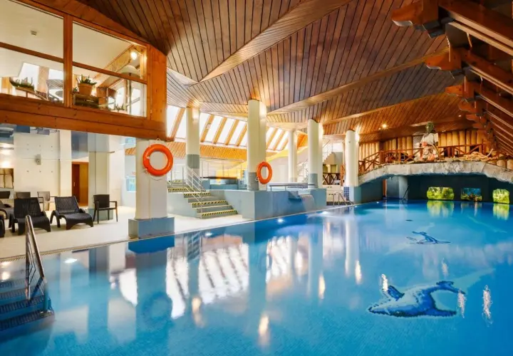 Basen w hotelu Belvedere Resort & Spa z drewnianym sufitem i mostkiem. Woda jest błękitna, a na dnie widoczne są ozdobne ryby.
