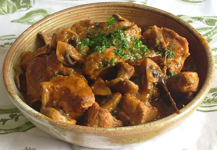 Un délicieux sauté de veau aux champignons, garni de persil frais, servi dans un bol en terre cuite.