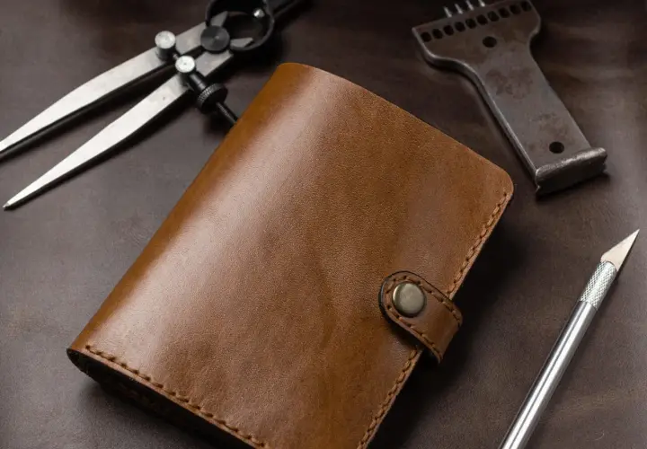 Brązowy portfel ze skóry, narzędzia do obróbki skóry: cyrkiel, dziurkacz, nożyk. Leather cuir to znaczy skóra.