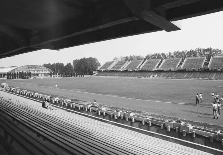Widok na stary stadion Stali Mielec z pustymi trybunami i boiskiem, gdzie trenuje kilku piłkarzy.