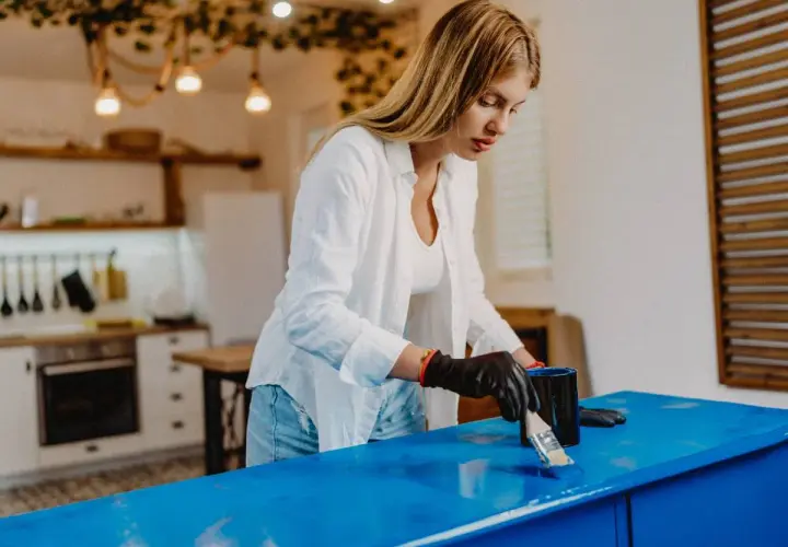 Donna con guanti neri applica vernice blu su un mobile, trasformandolo per rendere opaco un mobile lucido.
