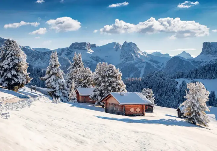 Chalets enneigés sous un ciel bleu, au cœur d'une **caravaneige massif central**. Sapins couverts de neige, montagnes majestueuses en arrière-plan.