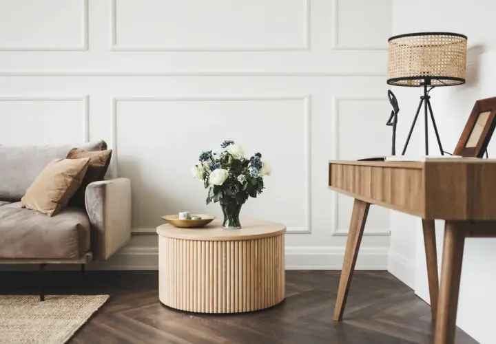 Elegancki salon w stylu klasycznym: beżowa sofa, drewniany stolik z bukietem róż, biurko i lampa z wiklinowym kloszem.