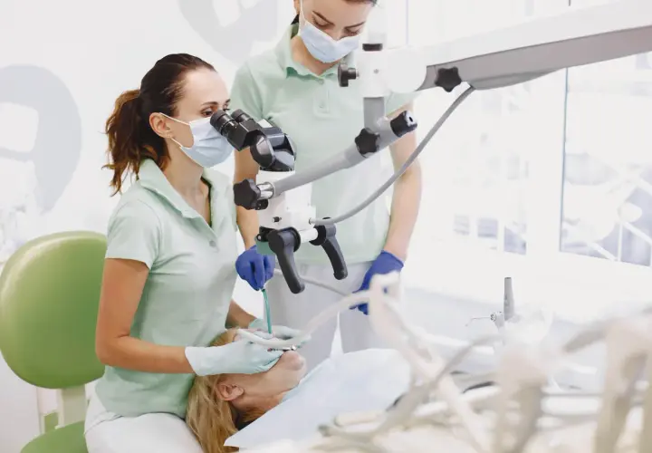 Dentystka z asystentką używają mikroskopu stomatologicznego, by skutecznie leczyć ból ósemki.
