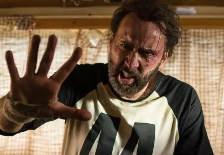 Nicolas Cage med blåmärken och svettig panna, höjer handen i en gest av stopp. En scen från en av hans filmer.