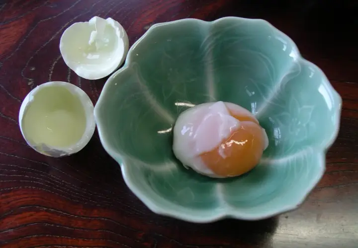 A perfectly soft-boiled egg, a delicacy of Japanese eggs, rests in a green, petal-shaped bowl.