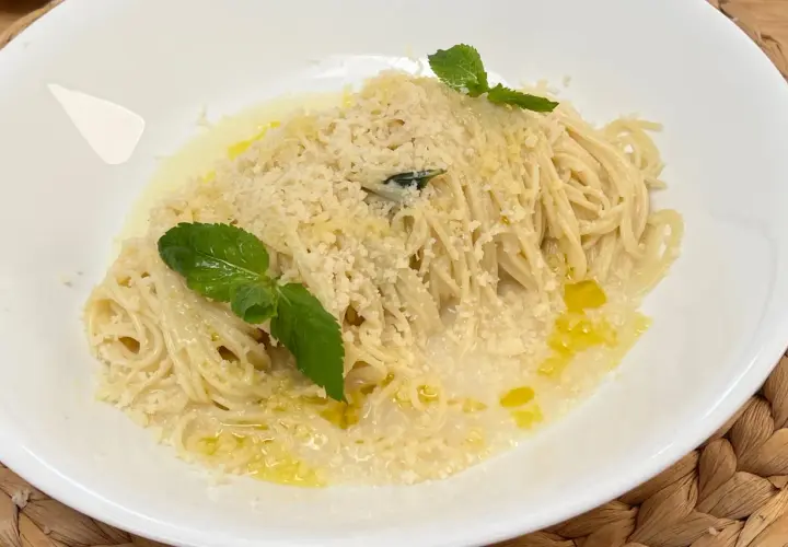 Spaghetti al limone cremosi, conditi con parmigiano grattugiato, olio d'oliva e guarniti con foglie di menta fresca.
