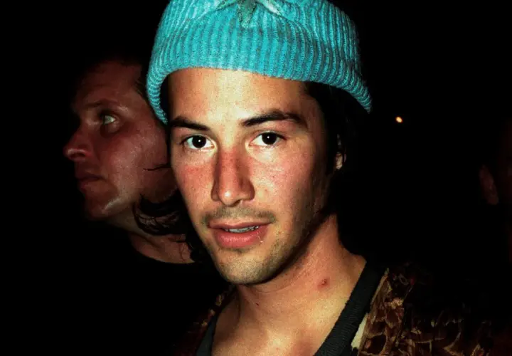 Młody Keanu Reeves w niebieskiej czapce, obok niego inny mężczyzna. Trudno zgadnąć, ile lat ma Keanu Reeves na tym zdjęciu.