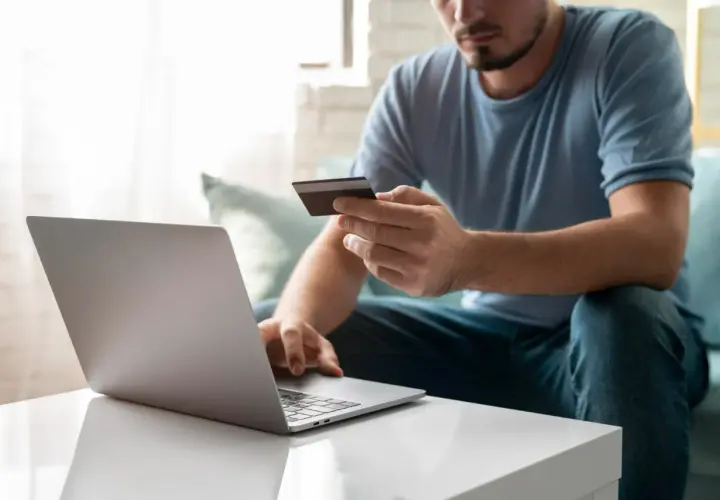 Mężczyzna z kartą kredytową przed laptopem, przygotowuje się, jak wpłacić pieniądze na PayPal.