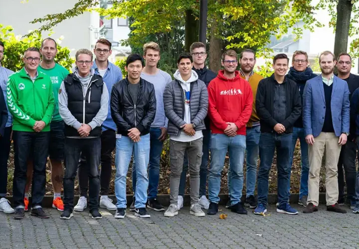 Eine Gruppe junger Männer steht lächelnd im Freien. Vielleicht sind sie angehende Fußball-Scouts, die ihre Ausbildung beginnen.