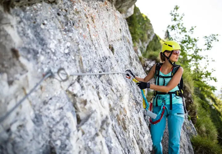 Kobieta w kasku i sprzęcie wspinaczkowym pokonuje via ferrata niemcy. Wspinaczka po skalnej ścianie z asekuracją.