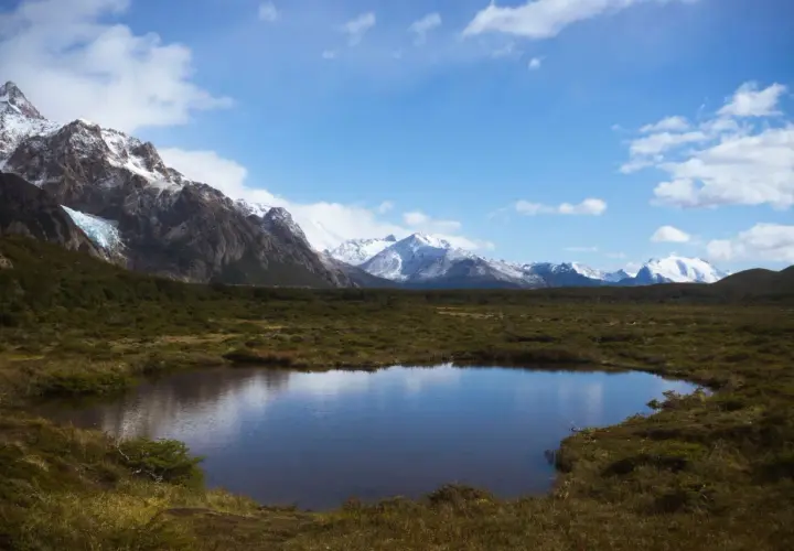 Spokojne jezioro odbija ośnieżone góry, w tym majestatyczne góry z Aconcagua, otoczone zielonymi wzgórzami pod błękitnym niebem.
