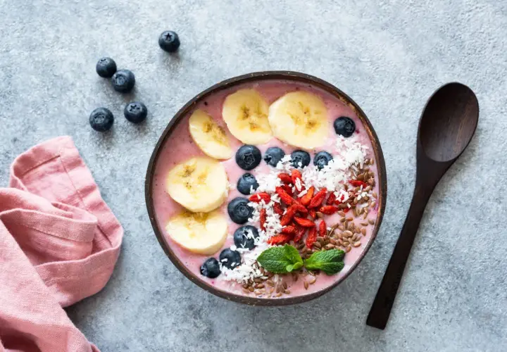 Kolorowa bowl z owocami: banan, borówki, jagody goji, wiórki kokosowe i siemię lniane. Idealna na zdrowe śniadanie, inspiracja z bowl przepisy.