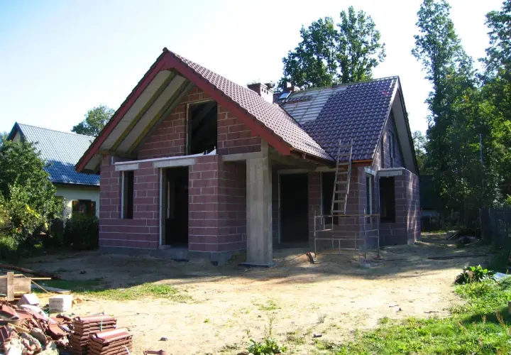 Budowa domu w toku, widoczne materiały budowlane i drabina. Może to być podstawa do obliczenia kary za samowolę budowlaną.